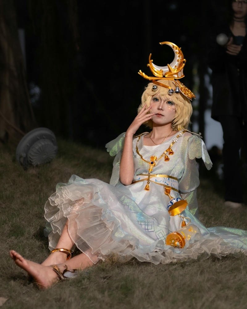Cosplayer nữ tóc vàng ngồi trên cỏ cầm trượng mặt trăng