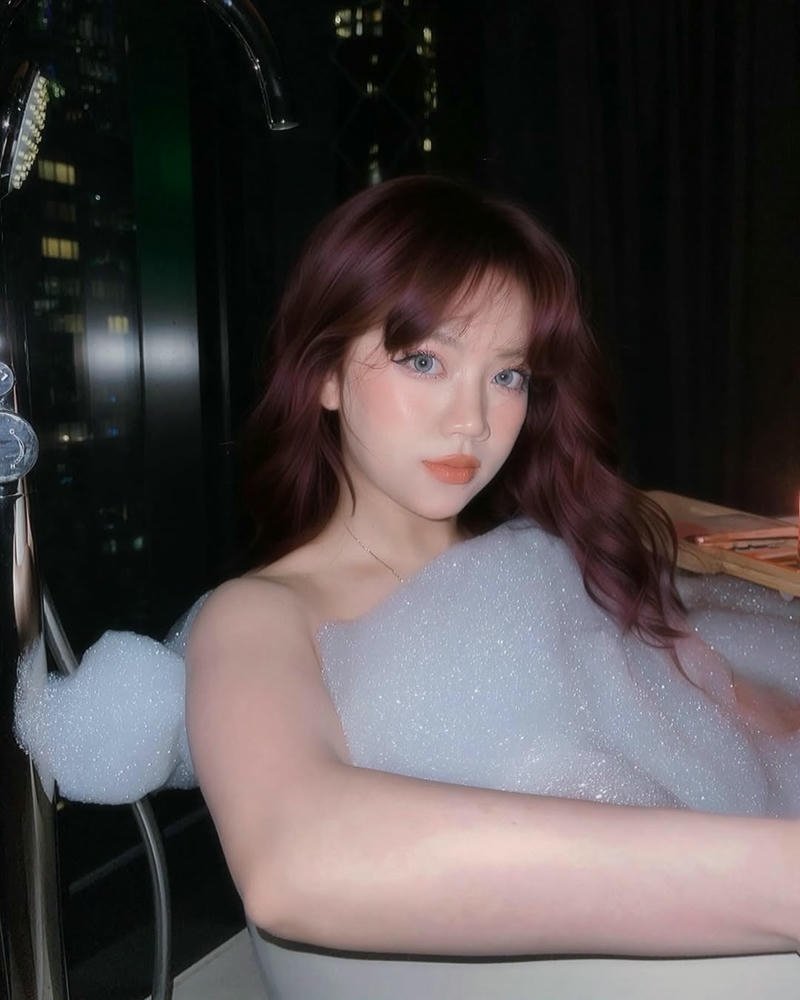 Helia xinh đẹp mặc áo trắng ngồi trong phòng ánh sáng tối