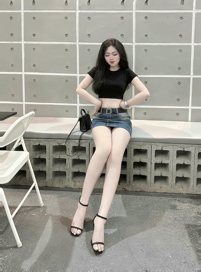 Gái xinh mặc váy ngắn jean đứng tựa vào tường trắng